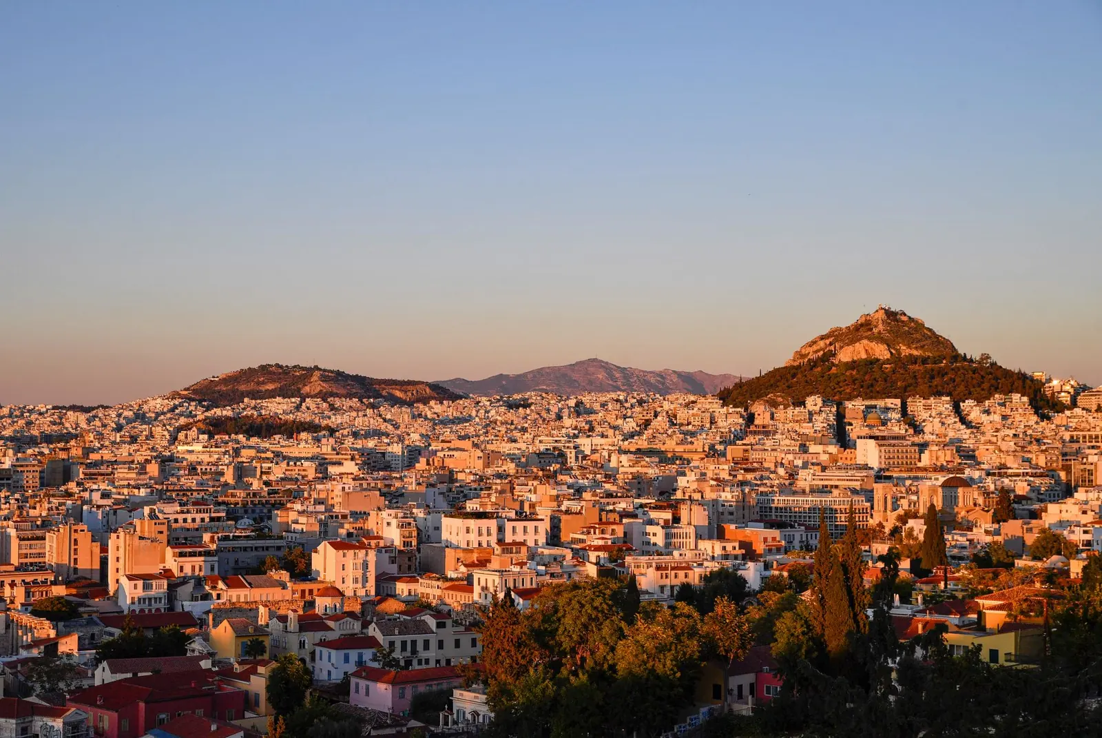 A breathtaking view of Athens cityscape at sunset with hills and historic architecture.