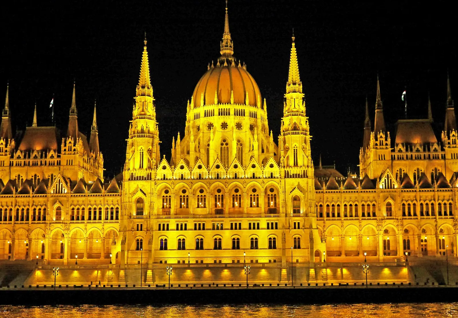 Illuminated Hungarian Parliament Building with reflection on Danube River at night.