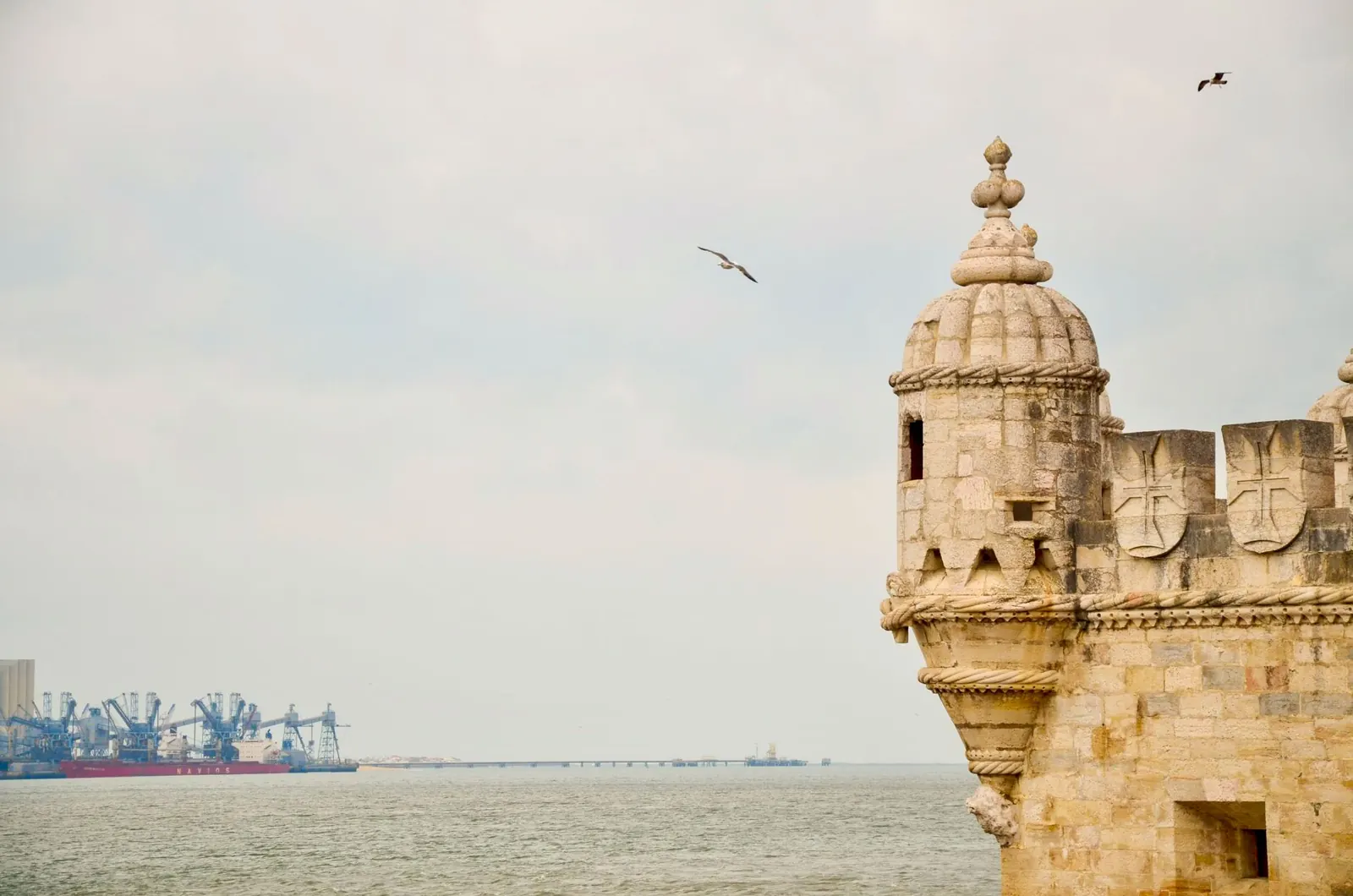 Scenic view of Belem Tower by the Tagus River in Lisbon, Portugal with birds in flight.