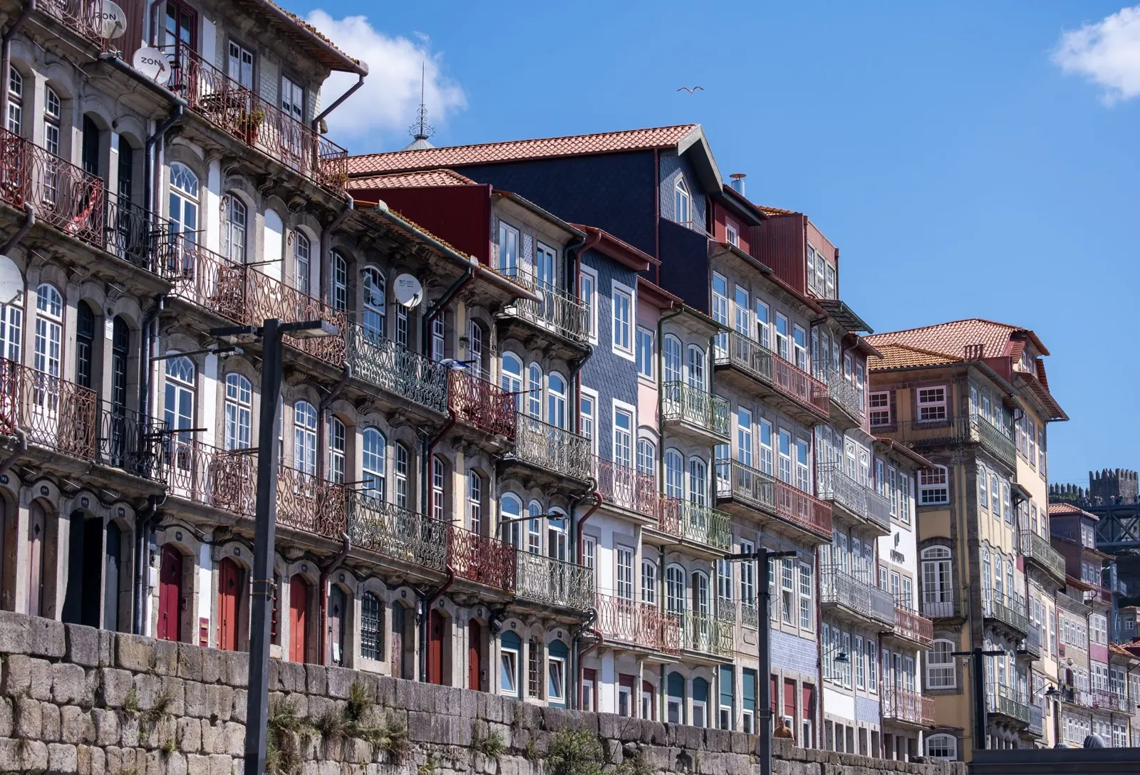 Vibrant, historic waterfront buildings along Porto's scenic riverfront under a clear blue sky.