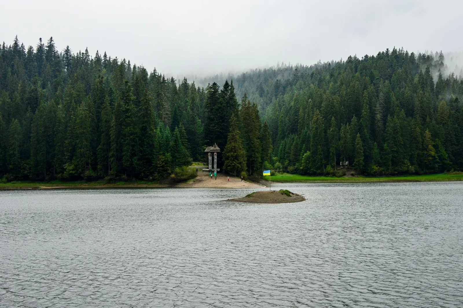 Misty morning at Synevyr Lake, Ukraine, surrounded by lush evergreen forest and tranquil waters.
