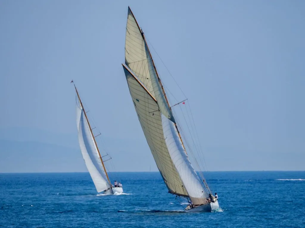 Two classic sailboats glide gracefully on blue ocean waters during a sunny day, showcasing maritime elegance.