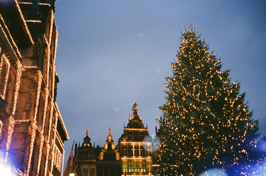 Sparkling lights adorn a Christmas tree in vibrant Antwerp, Belgium, with historic architecture in the backdrop.