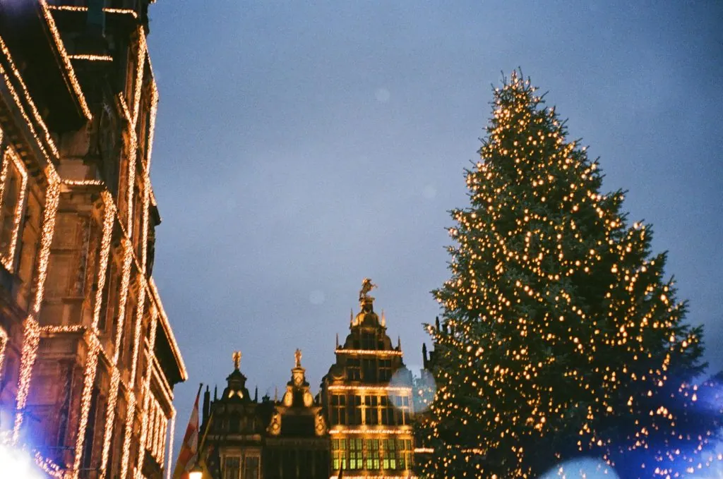 Sparkling lights adorn a Christmas tree in vibrant Antwerp, Belgium, with historic architecture in the backdrop.