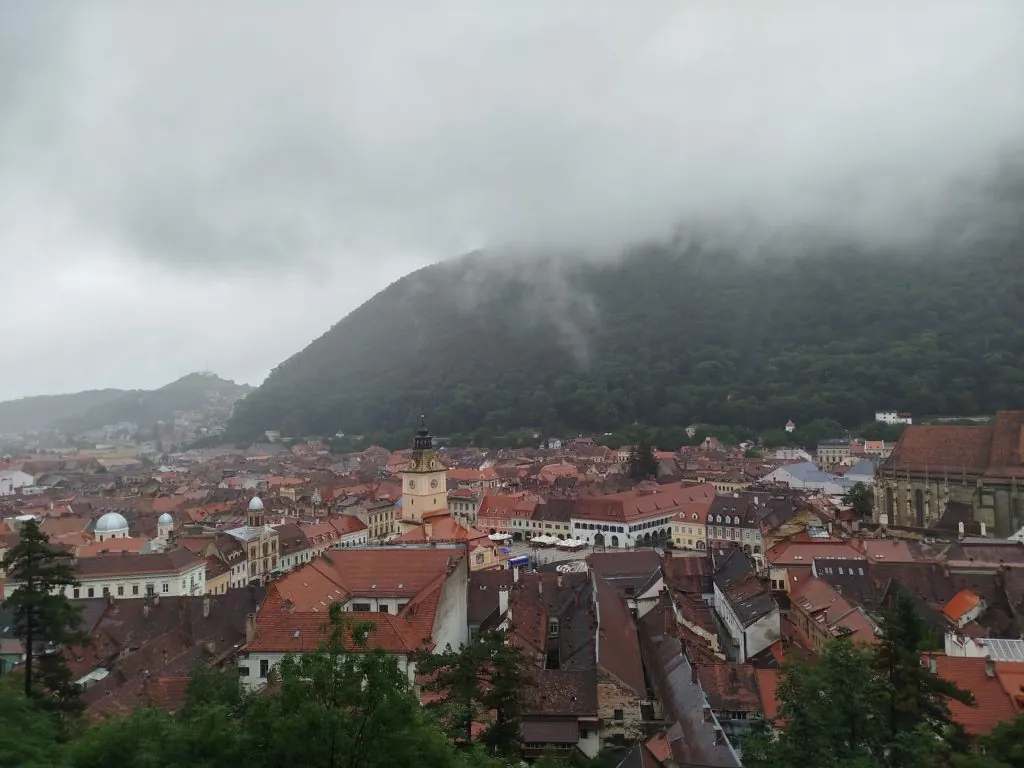 Aerial view of Brașov, Romania, showcasing historic architecture and Mount Tâmpa under a cloudy sky.