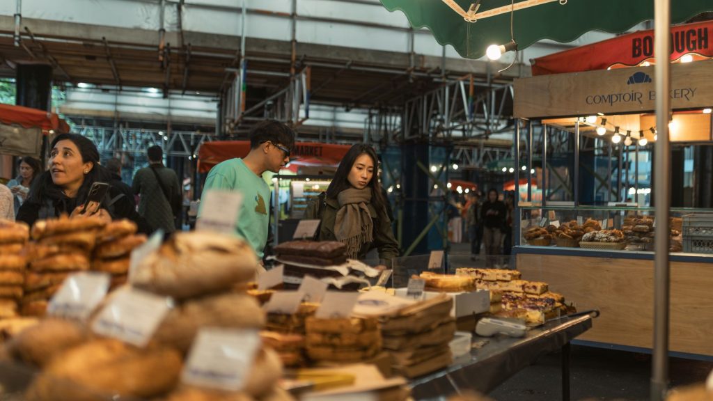 Candid shoppers exploring baked goods at an outdoor market stall during autumn.