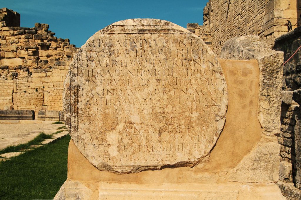 Detailed view of ancient Roman stone with inscriptions, under clear sky.