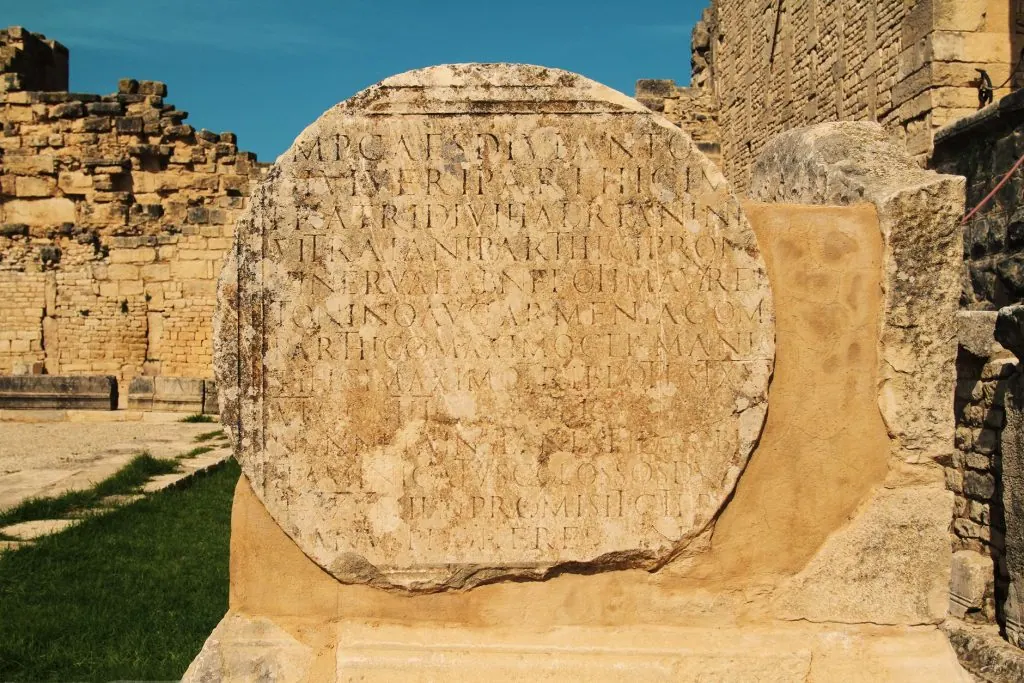 Detailed view of ancient Roman stone with inscriptions, under clear sky.