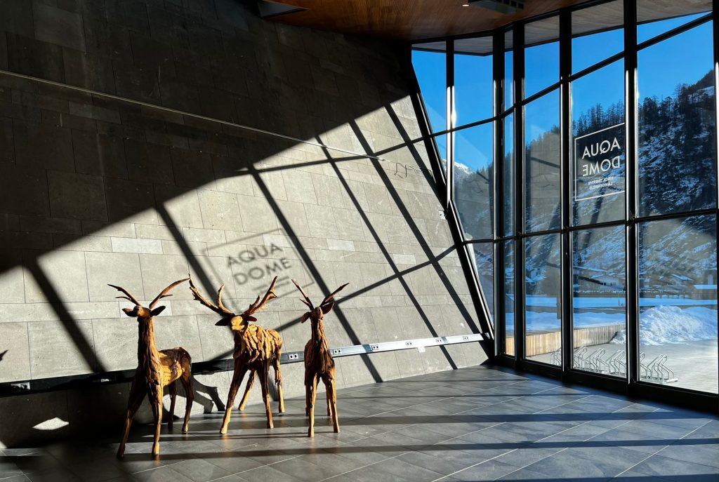 Wooden deer sculptures casting shadows in modern Alpine resort Aqua Dome with snowy mountain view.