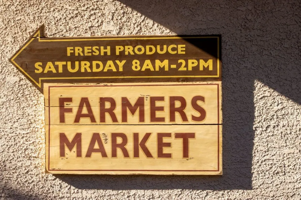 Brightly painted farmers market sign indicating fresh produce times.