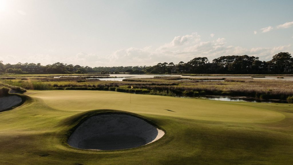 A picturesque view of a golf course in Kiawah Island, SC, showcasing lush greens, water features, and a serene sunset.