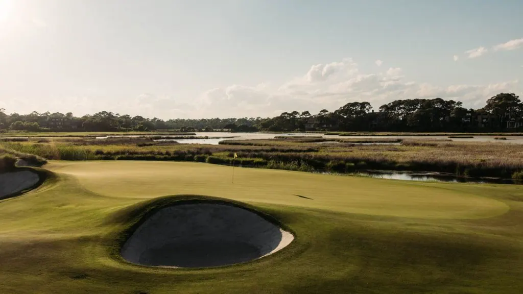 A picturesque view of a golf course in Kiawah Island, SC, showcasing lush greens, water features, and a serene sunset.