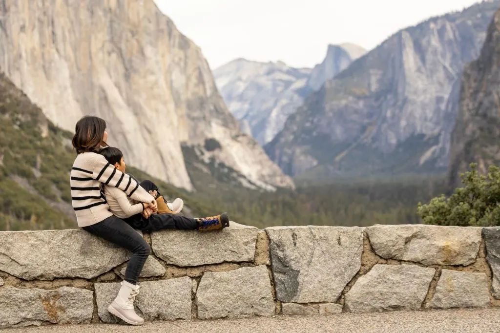 A mother and child sitting on a stone wall, enjoying the breathtaking view of Yosemite's iconic landscapes.