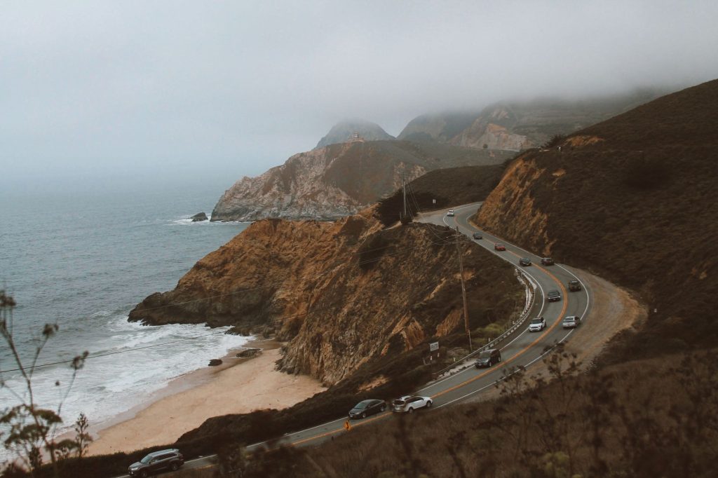 Aerial view of a winding coastal road embracing the foggy cliffs by the ocean.