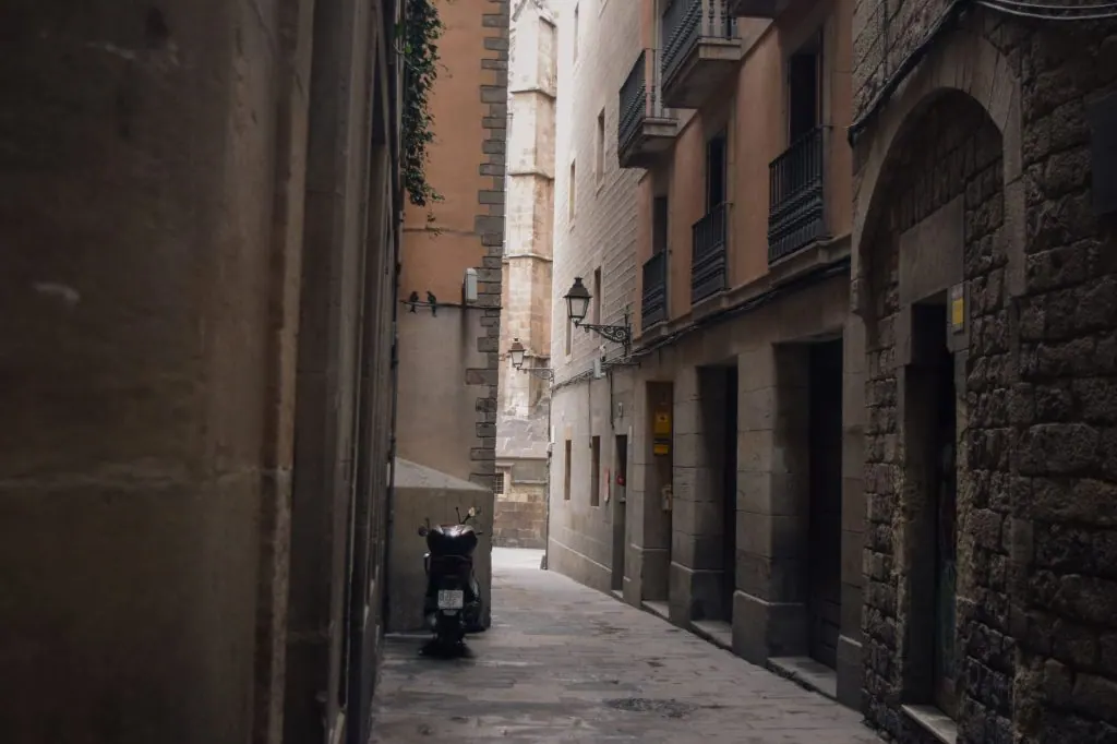 A quiet, narrow alley in Barcelona featuring a parked motor scooter and historic buildings.