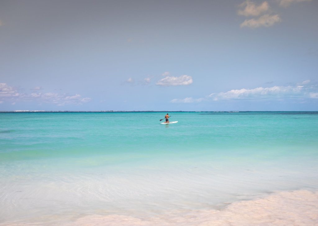 A man enjoys paddleboarding on the serene turquoise waters of Cancún, México under a clear sky.