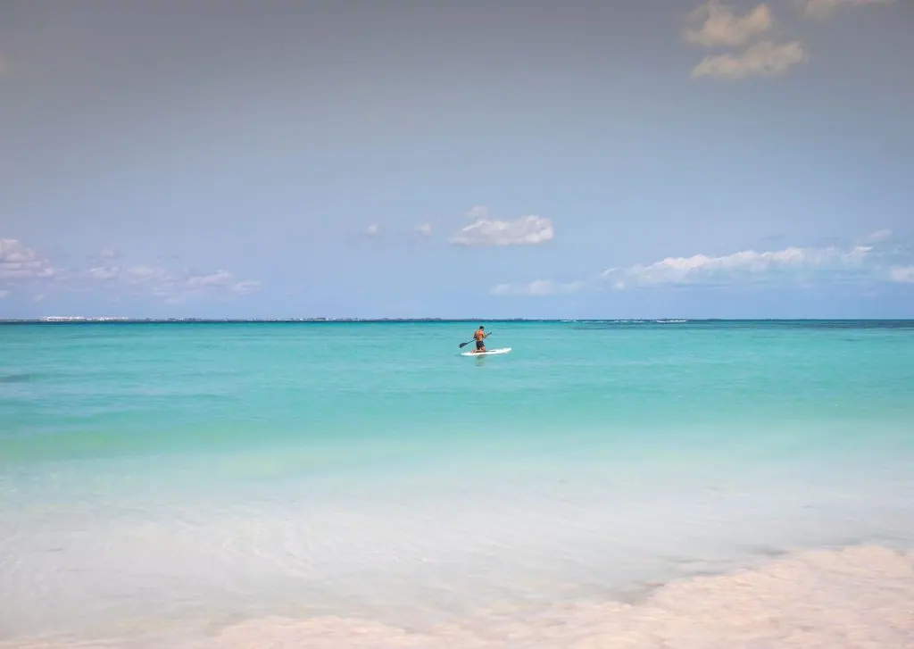A man enjoys paddleboarding on the serene turquoise waters of Cancún, México under a clear sky.