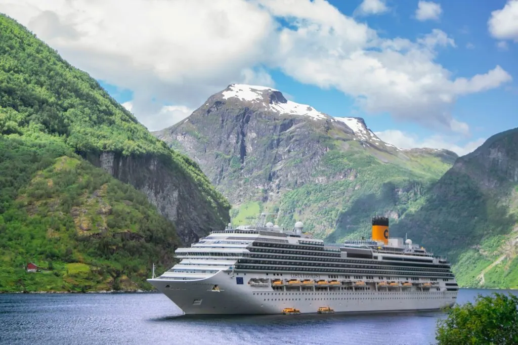 A grand cruise ship navigates the serene Geiranger Fjord in Norway, surrounded by majestic mountains.