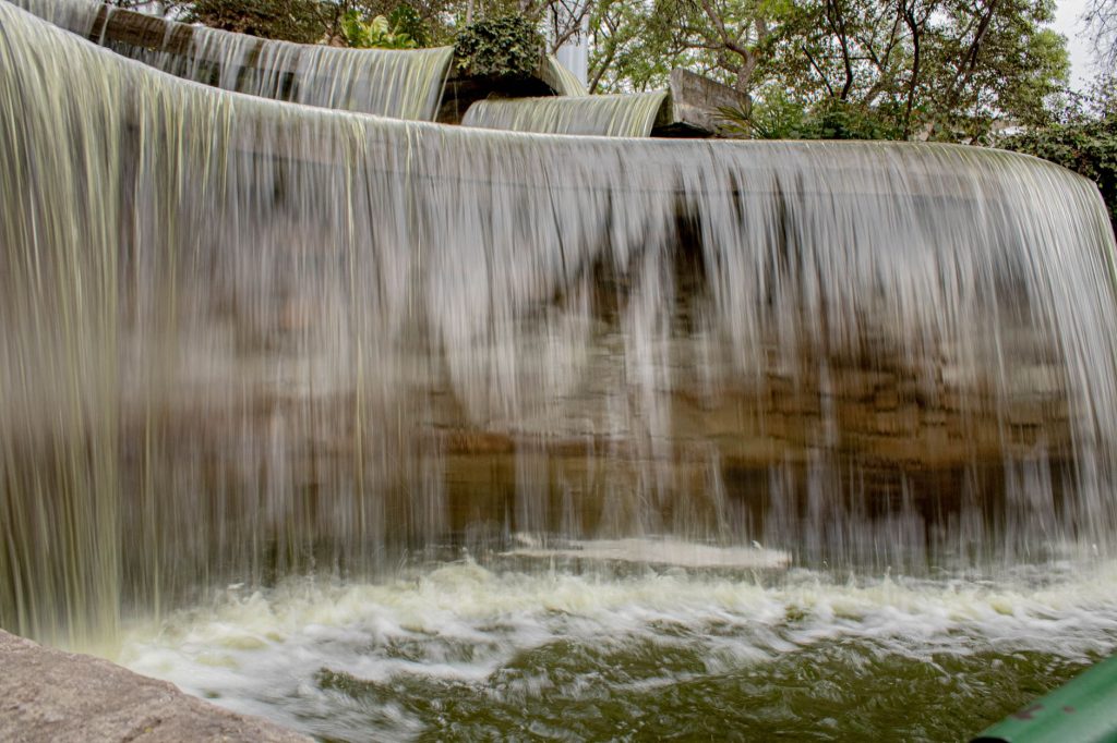 A tranquil park waterfall with cascading water, surrounded by greenery, creating a peaceful atmosphere.