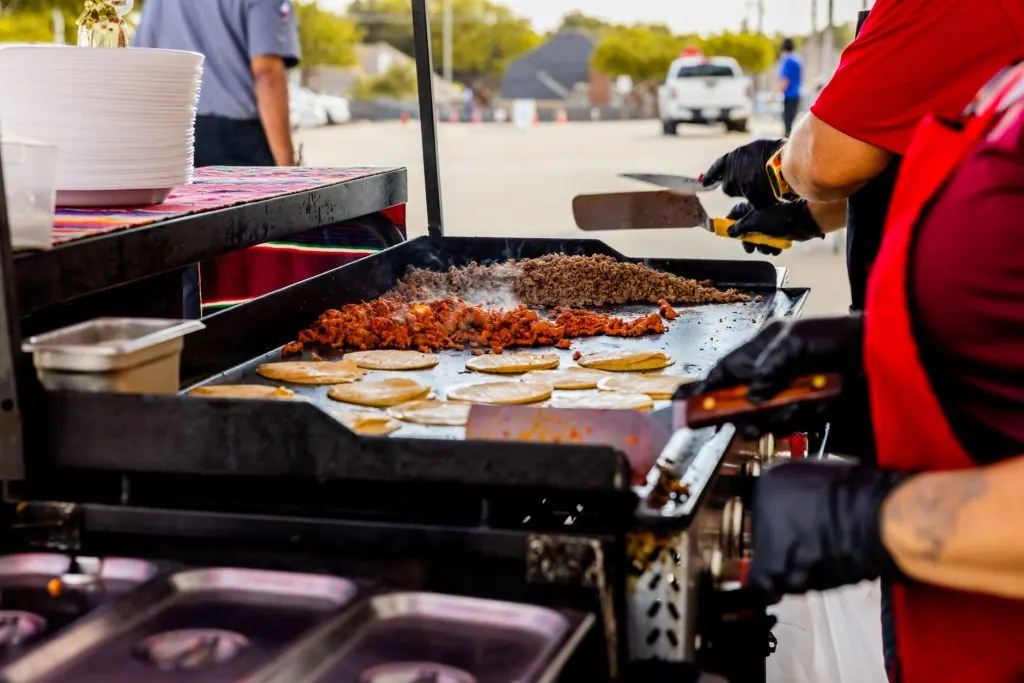 A street vendor prepares authentic Mexican tacos on a griddle with fresh ingredients.