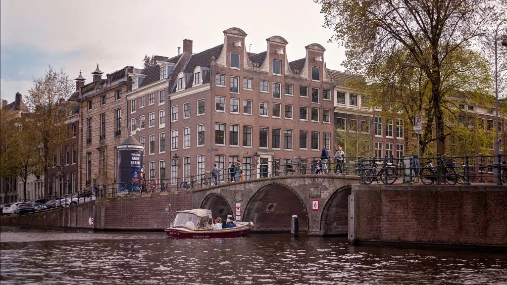 Charming Amsterdam scene with historic buildings, a bridge, and a canal boat.