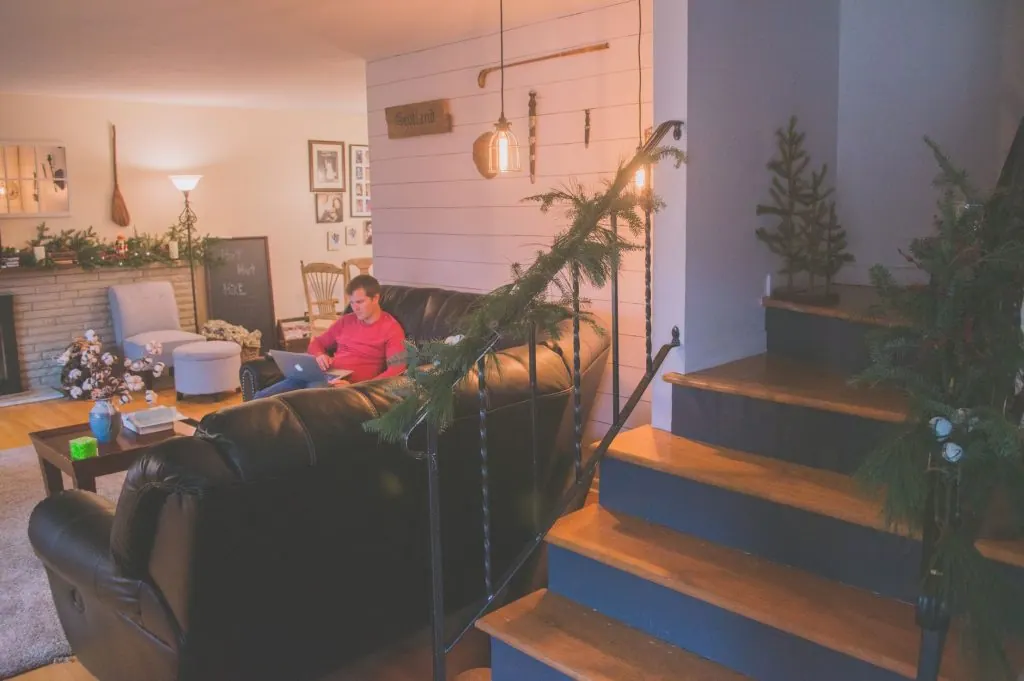 A cozy living room adorned with holiday decor, featuring a person working remotely on a laptop.