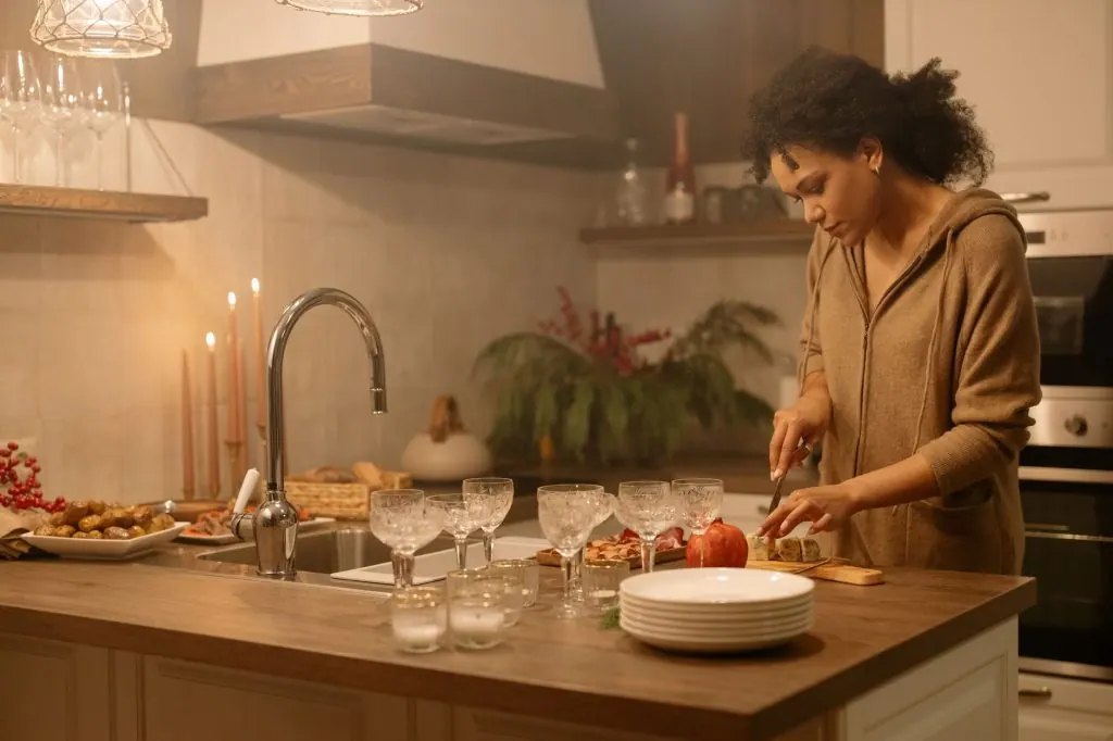 A woman in a brown jacket slices food in a cozy kitchen setting, enhancing a warm and homely atmosphere.