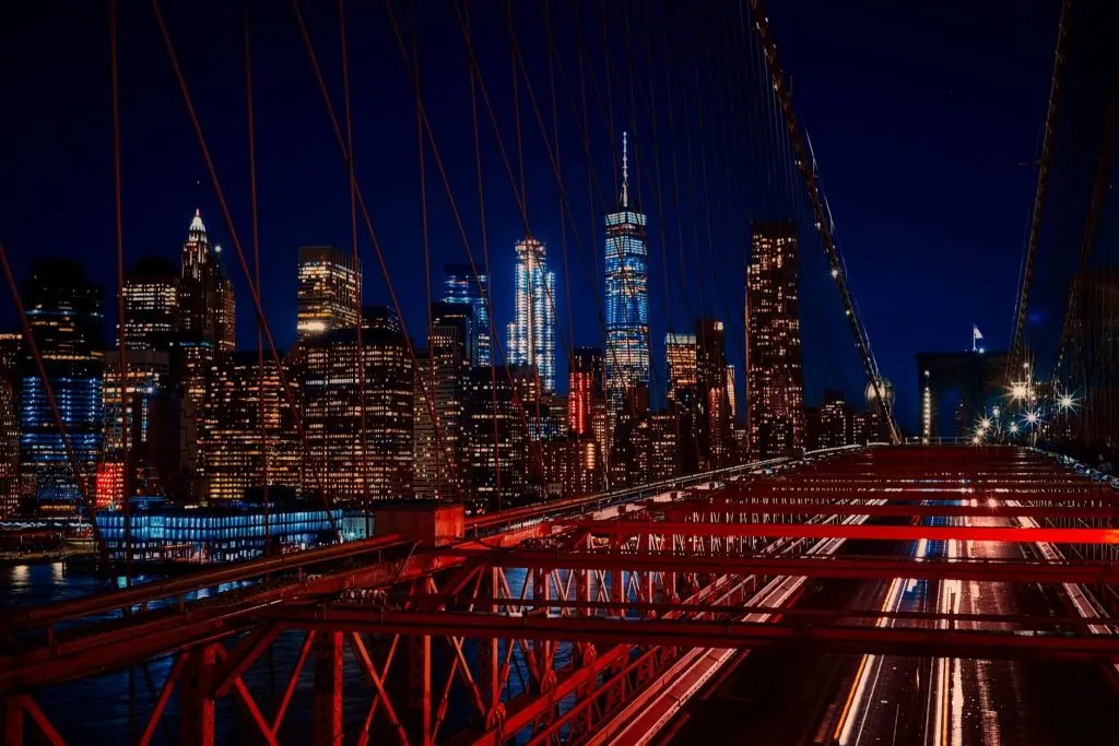 A breathtaking night view featuring the New York City skyline and iconic Brooklyn Bridge illuminated in vibrant colors.