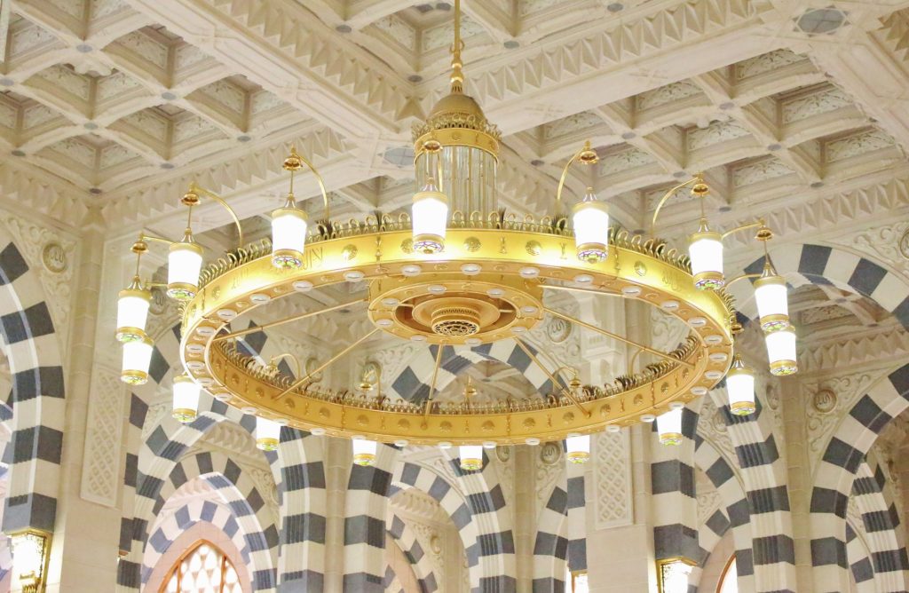 Stunning view of a golden chandelier in a richly decorated mosque interior.