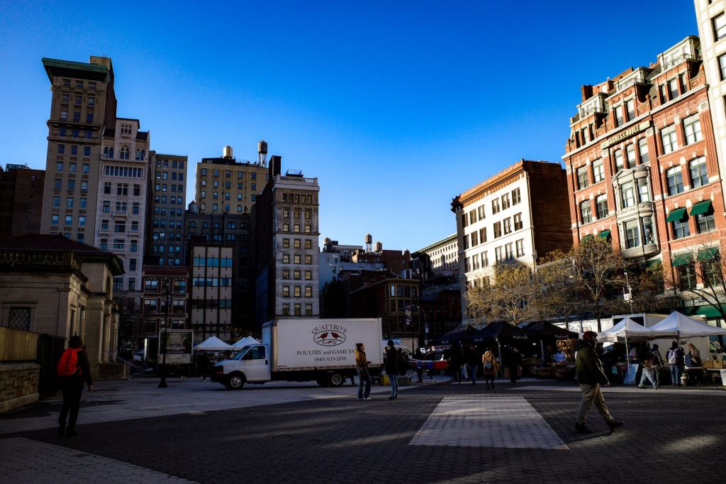 A vibrant scene of people and buildings in Union Square, NYC under a clear blue sky.