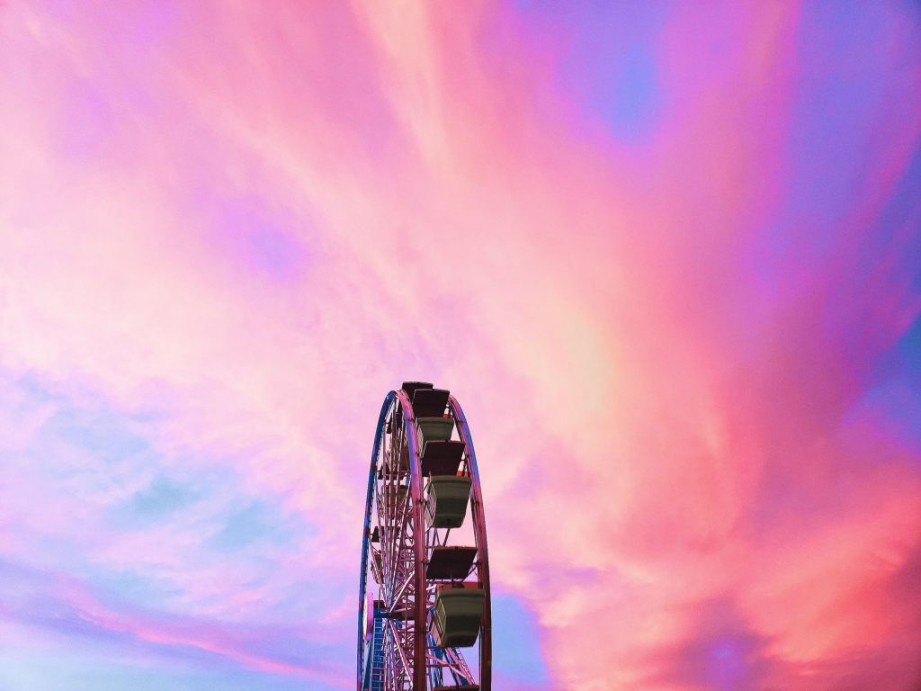 Ferris wheel silhouetted against vibrant pink and purple sky at sunset.