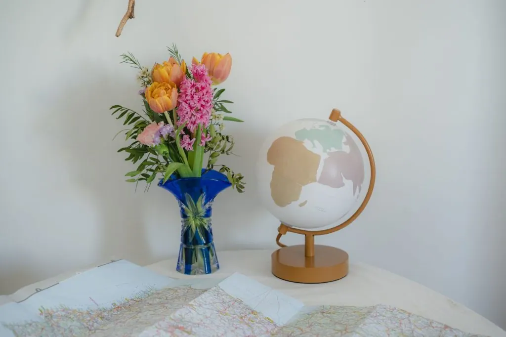 A vibrant flower bouquet in a blue vase beside a globe on a table.