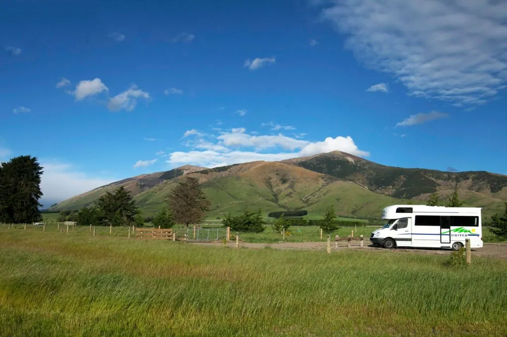 A recreational vehicle parked in a picturesque countryside setting with mountains in the background.