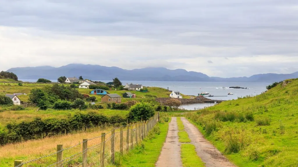Scenic view of a coastal village in Scotland with lush greenery and distant mountains.
