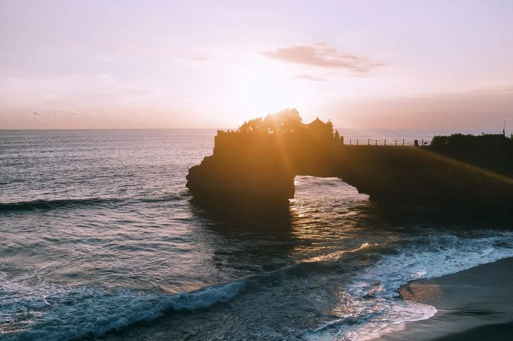 Amazing seascape with bright sunset through trees growing on rocky formations and promenade path in summer evening