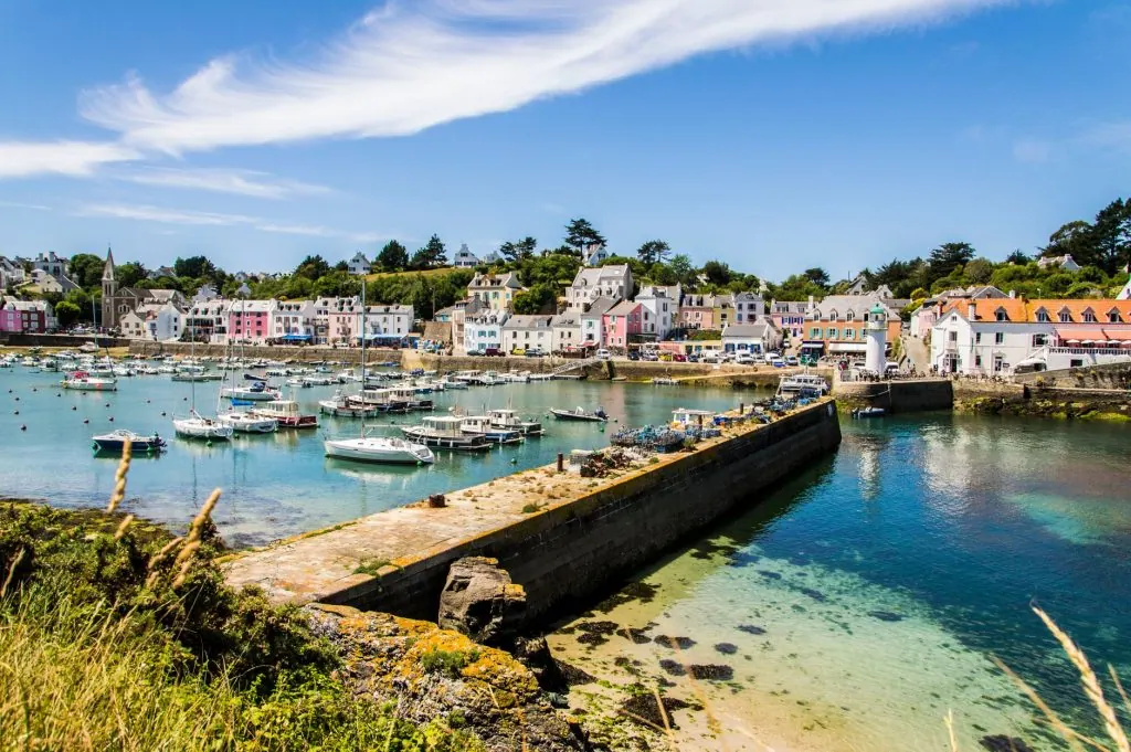 A picturesque marina scene with moored boats and colorful seaside town under a clear sky.
