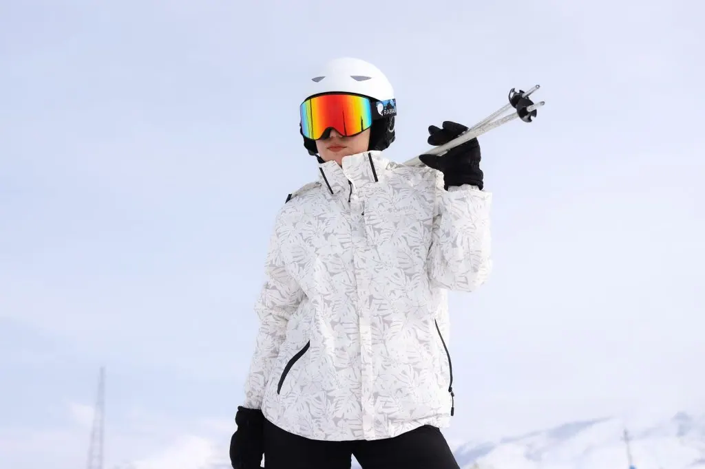 Adult skier in white gear on a bright snow-covered mountain holding ski poles, ready for adventure.