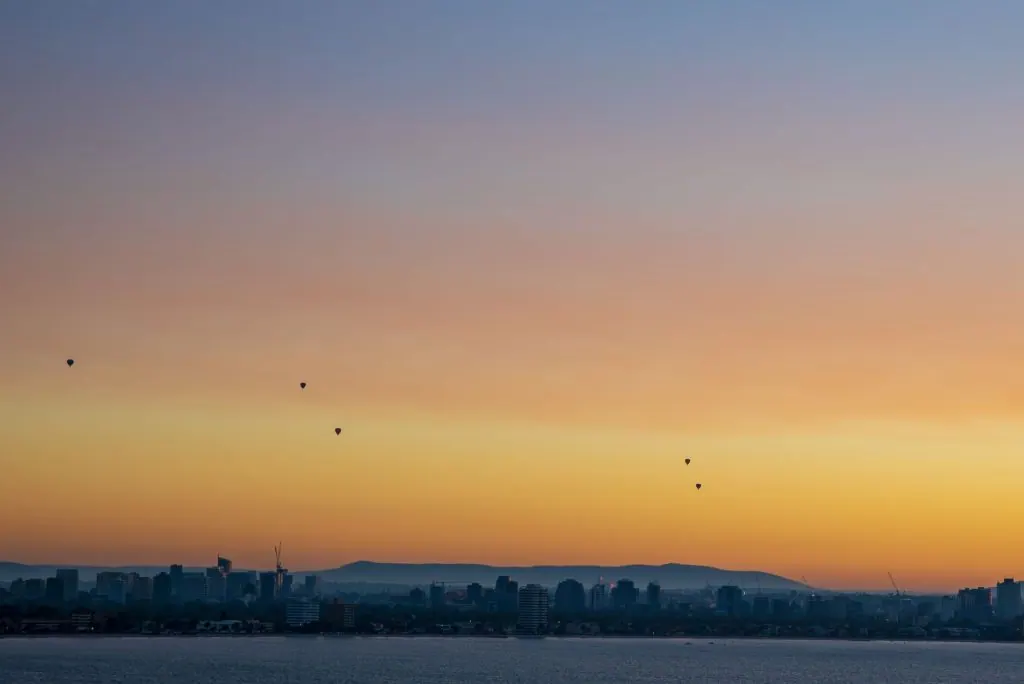 A breathtaking view of hot air balloons gliding over Melbourne's skyline during a serene sunrise.