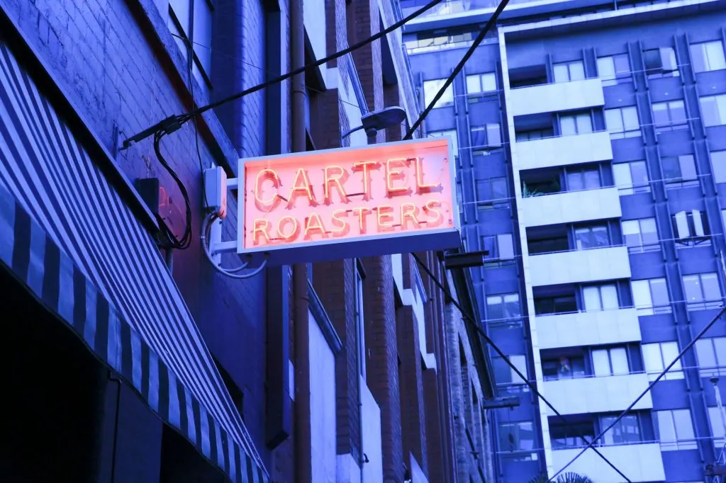 A vibrant neon sign for 'Cartel Roasters' in a Melbourne alleyway, showcasing urban cityscape charm.
