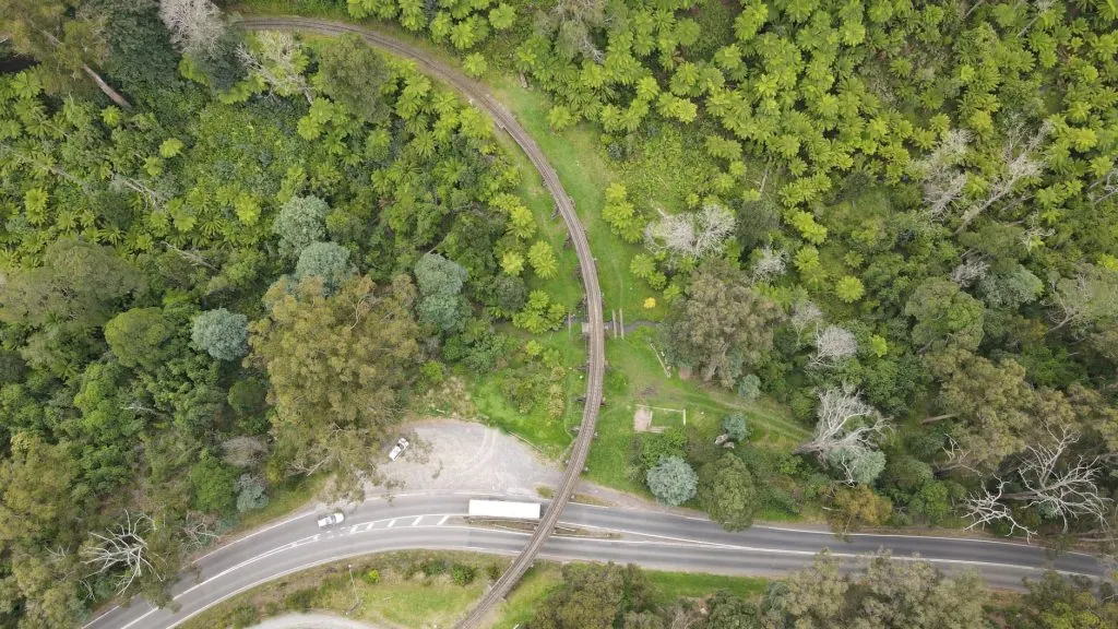 Aerial view of scenic railway tracks and road amidst lush green forest in Belgrave, VIC, Australia.