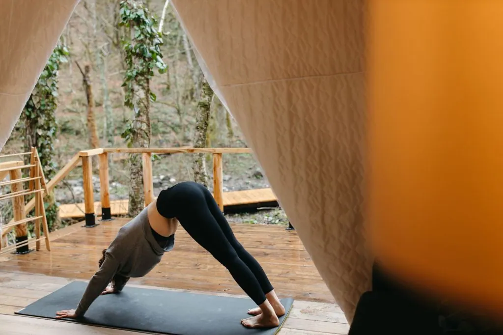Woman practicing yoga outdoors in a tent, emphasizing relaxation and fitness.