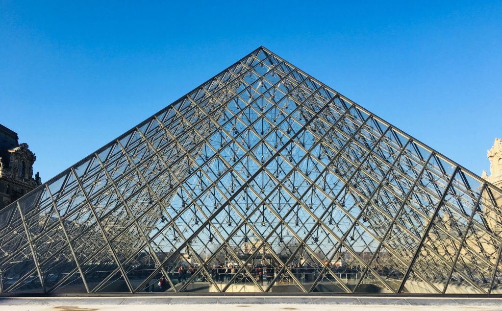 Iconic glass pyramid at the Louvre Museum in Paris reflecting a vibrant blue sky.