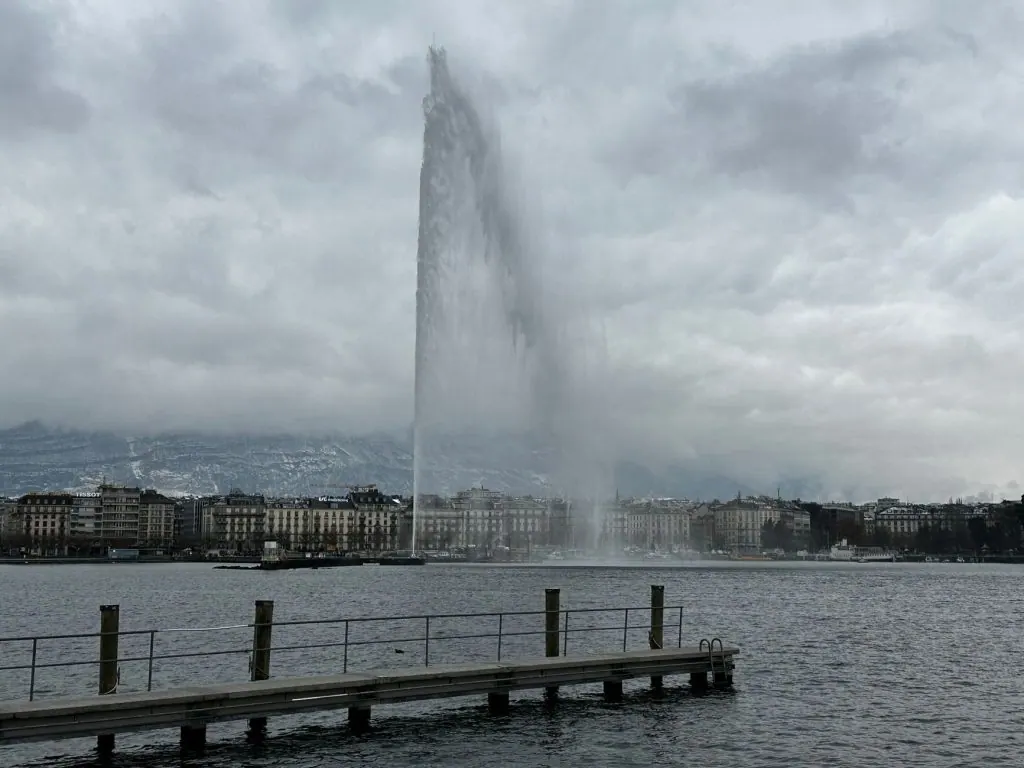 View of the iconic Jet d'Eau fountain in Lake Geneva against a cloudy skyline.