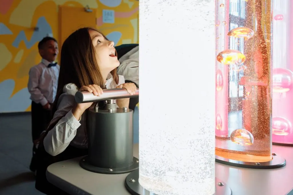 Children engage with interactive science exhibit featuring colorful liquids and lights.