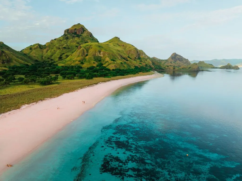 Aerial view of the pink beach on Padar Island, surrounded by lush green hills and turquoise waters.