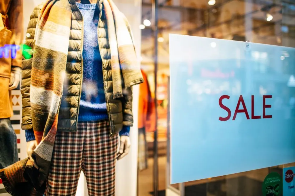 Mannequin display of winter fashion with sale sign in a clothing store window.