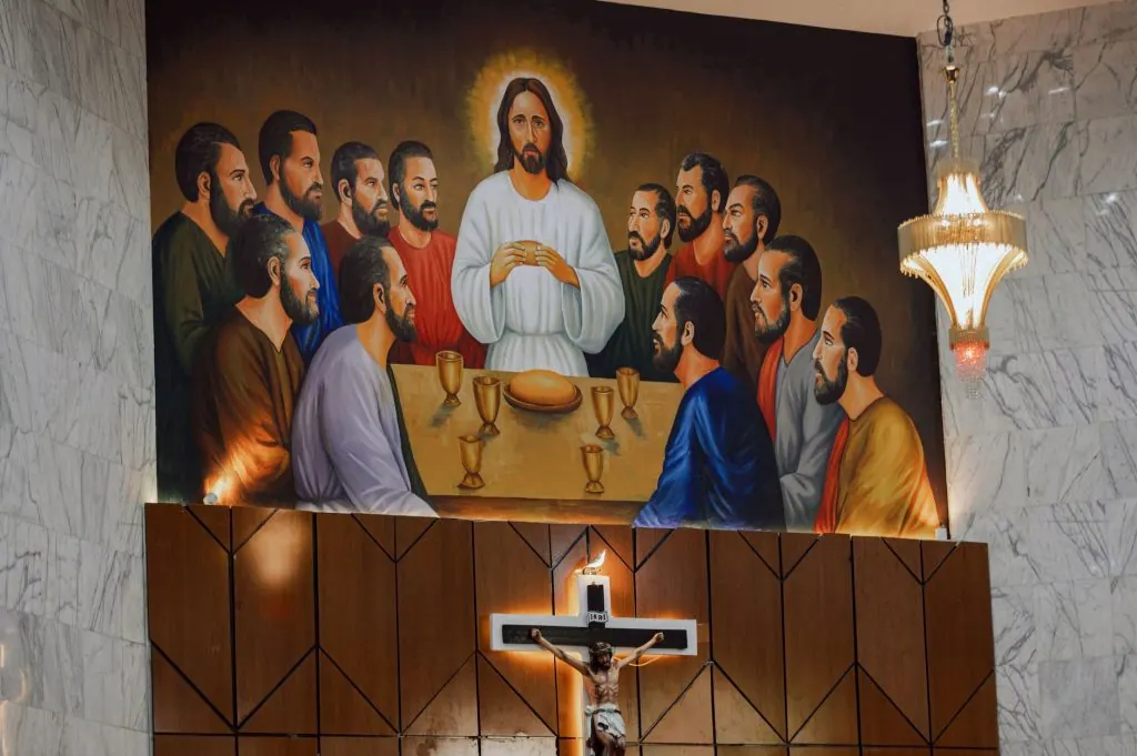 Vibrant mural of The Last Supper displayed in a church with chandelier and crucifix.
