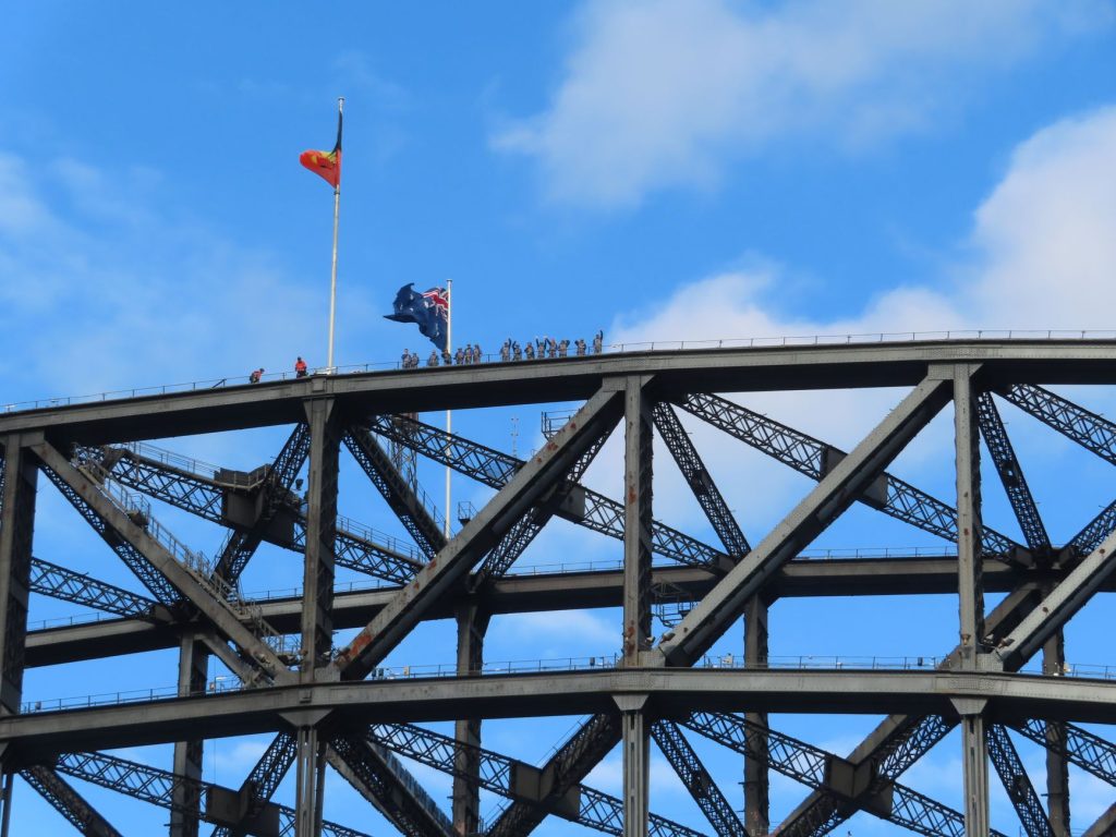 Sydney Harbour Bridge showcasing climbers and Australian flag against blue sky.