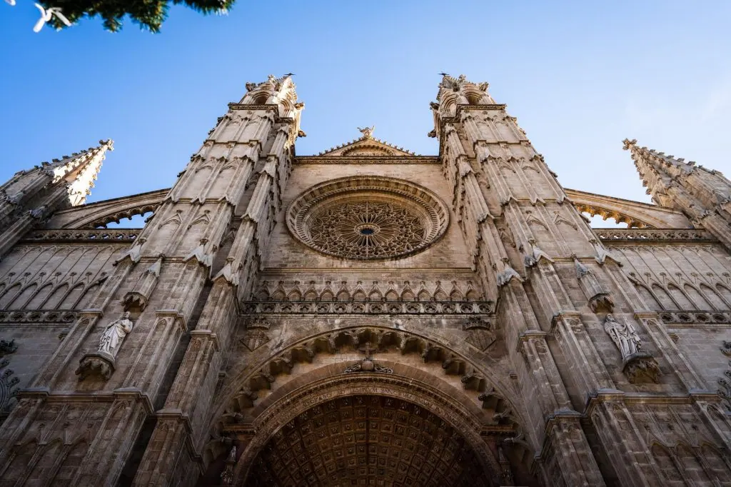 Epic low angle shot capturing La Seu Cathedral's grand gothic architecture against a blue sky.