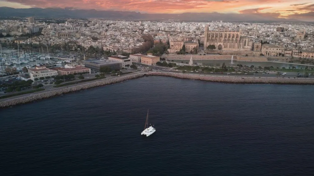 Stunning aerial view of Palma Cathedral and cityscape with a yacht during sunset.